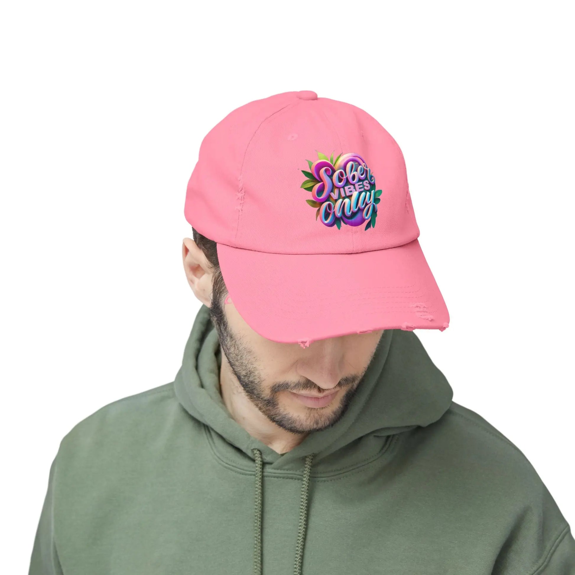 Person wearing a pink cap with colorful text and a green hoodie on a white background
