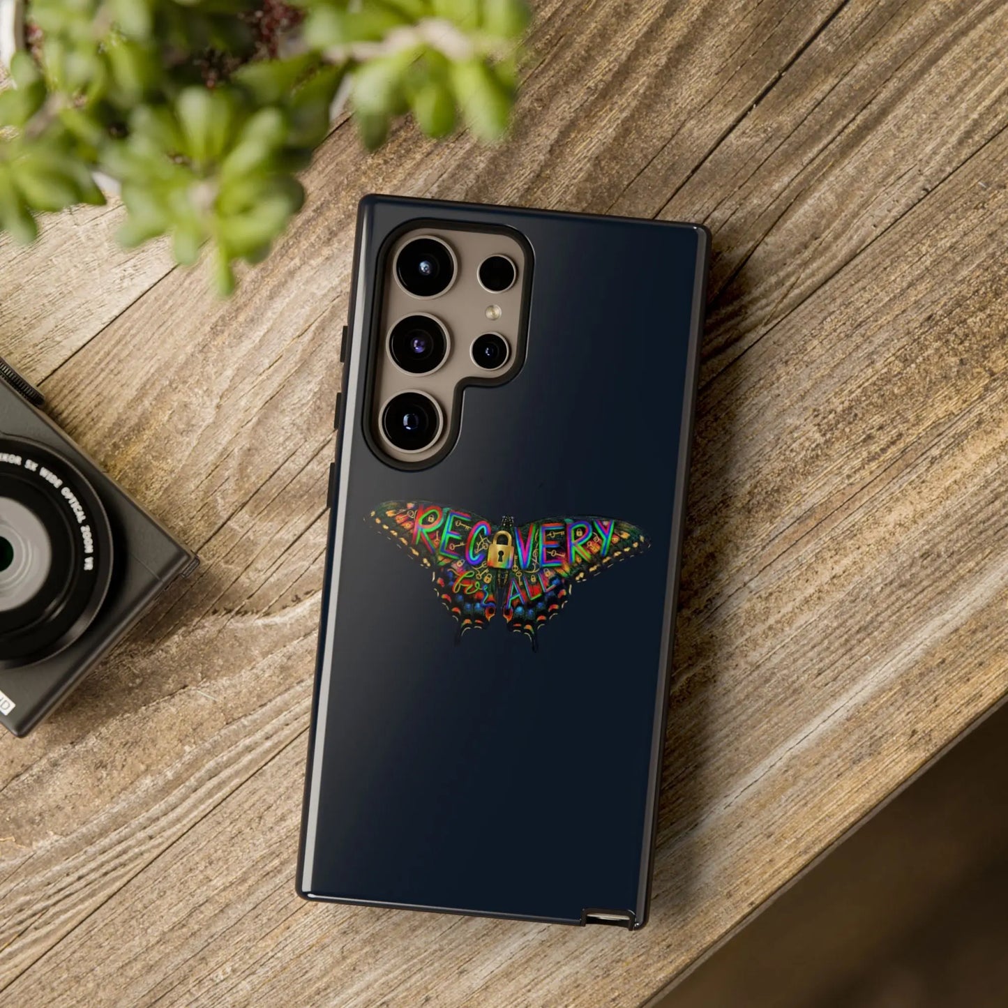 Phone case with butterfly design and 'RECOVERY' text on a wooden surface